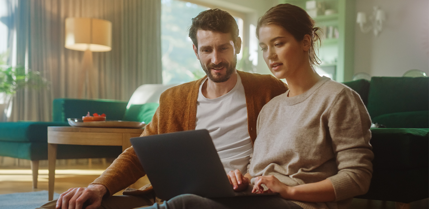 A man and a woman are sitting on a sofa looking at a tablet screen.