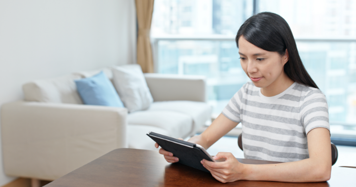 A woman is sitting at home and watching something on her tablet.