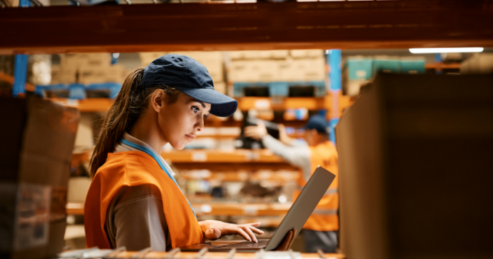 A woman in a warehouse is working on a laptop.