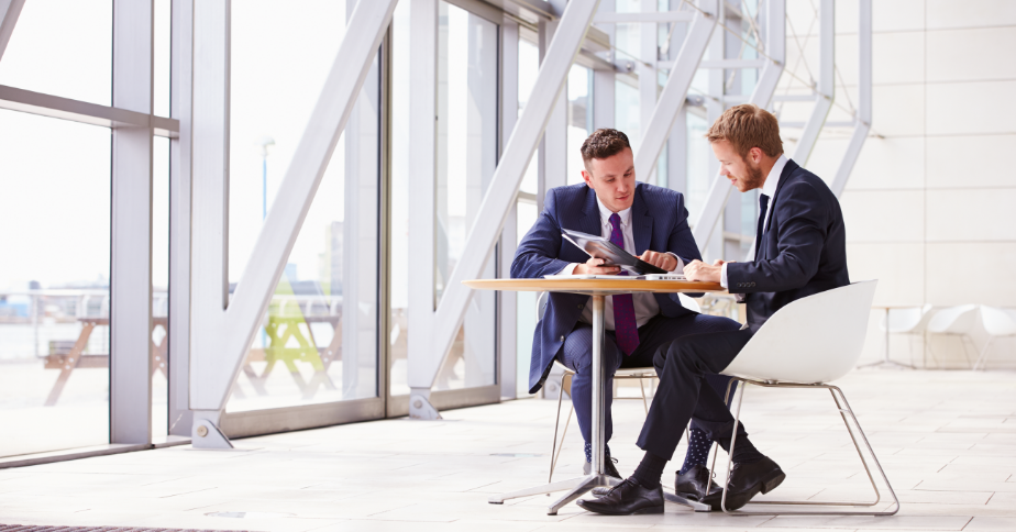 Two men dressed in suits are talking to each other with documents in their hands.