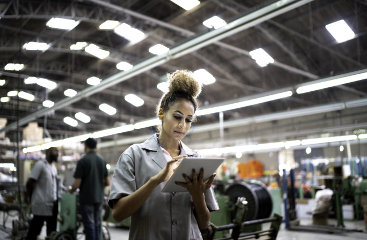 A woman is working on her tablet. She is in a factory.