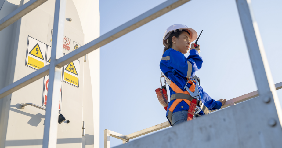 A woman wearing a safety suit speaks into a walkie-talkie