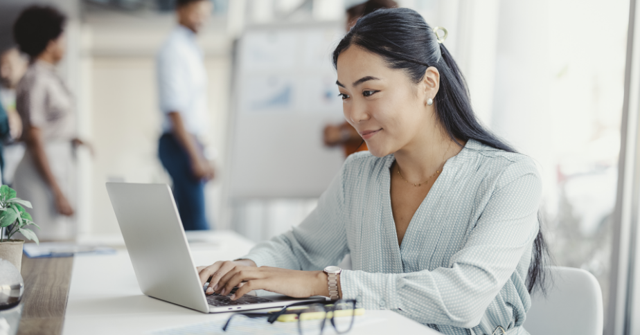 A woman smiles as she looks through her laptop.