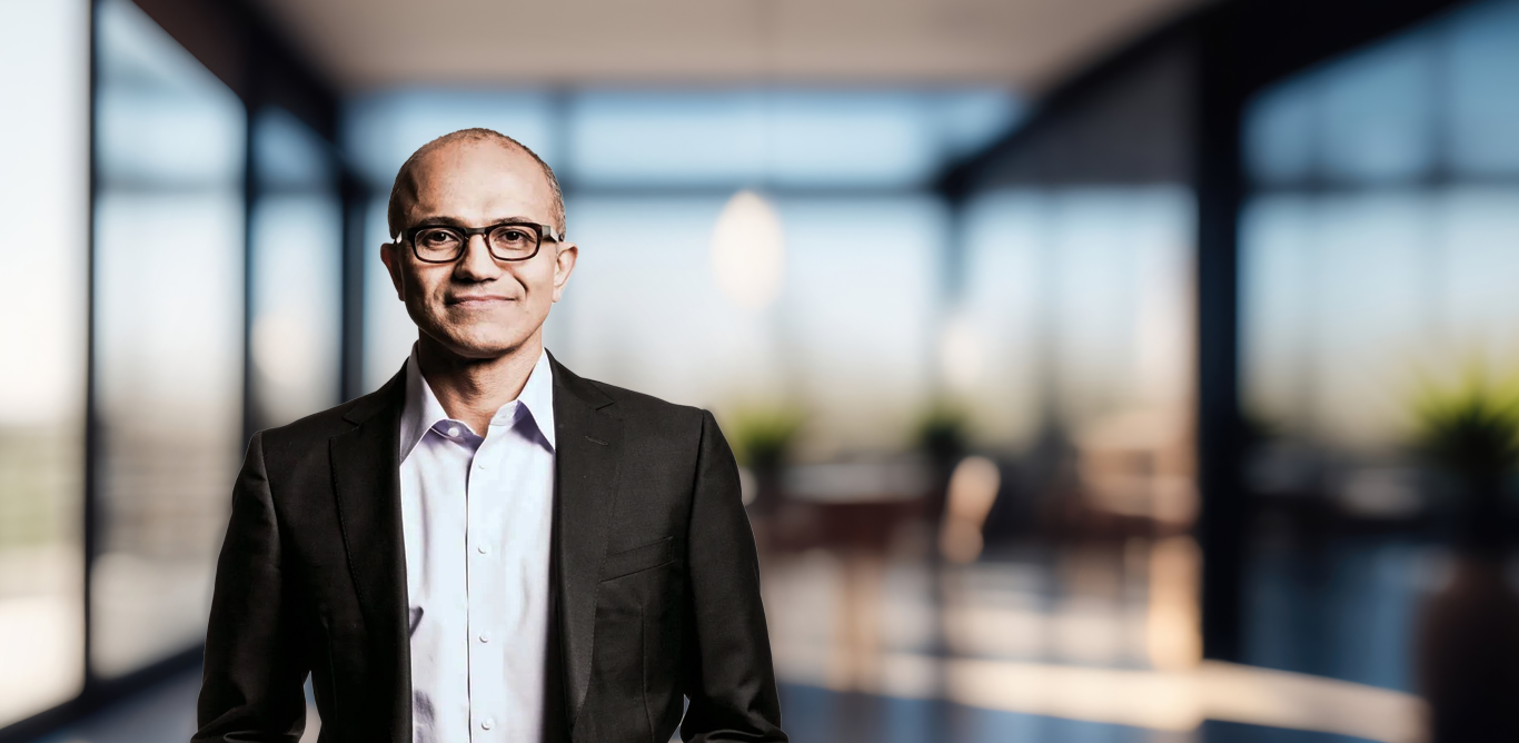 Satya Nadella is looking into the camera and is gently smiling.