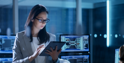A bespectacled woman is looking down at a screen.