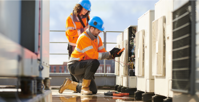 A woman and a man wearing safety helmets and jackets are on a rooftop working on something.