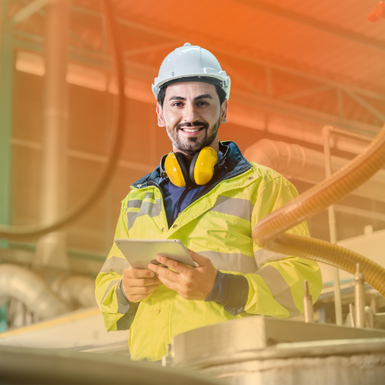 A construction worker is looking at the camera and smiling. He is holding a tablet.