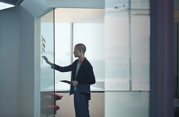 A business woman is standing, thinking, and sticking notes on a glass screen.